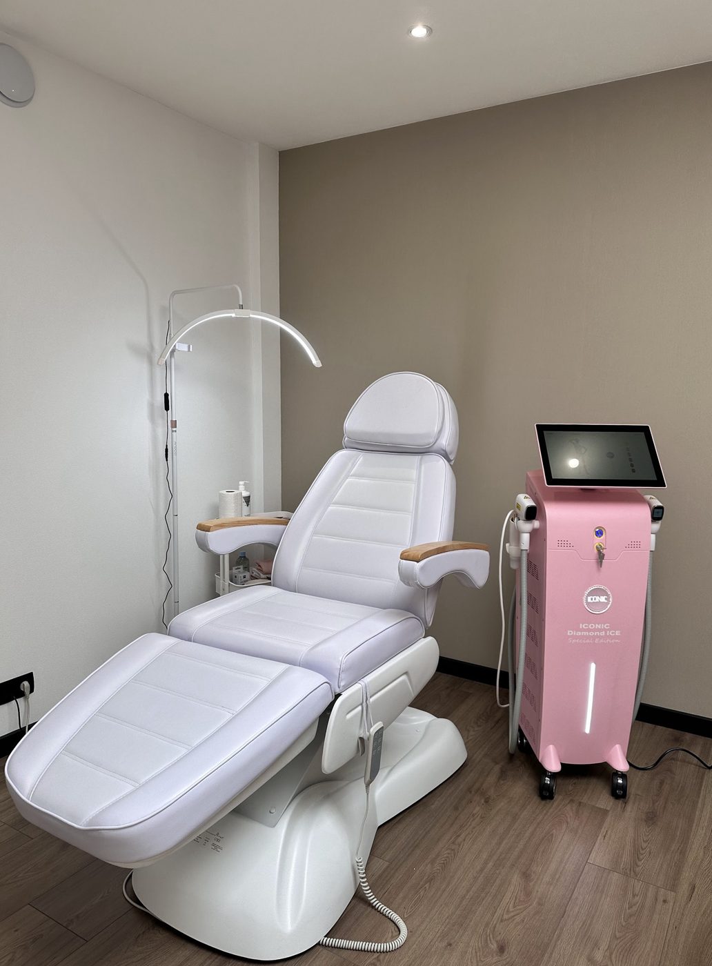 De lichte behandelkamer met een witte behandelstoel, een ringlamp en de roze ICONIC-laser